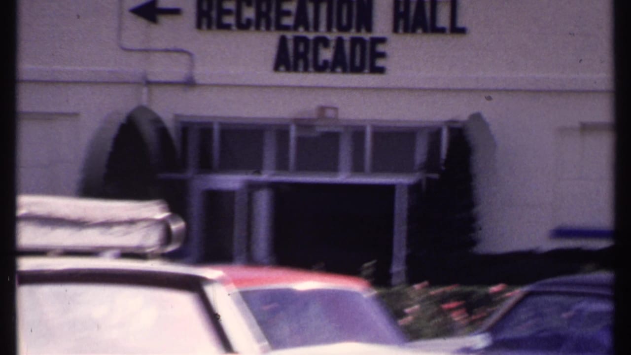 Parking lot cars in front of a white building with a Recreation Hall Arcade sign.