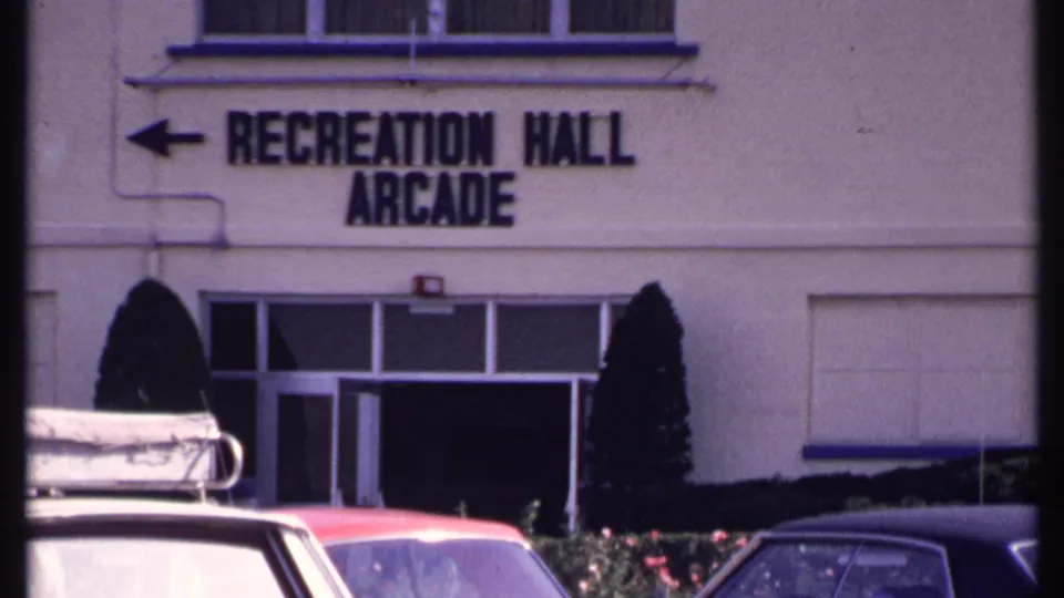 New London Recreation Hall Arcade exterior with directional sign, doorway, shrubs, and 1960s parked cars.