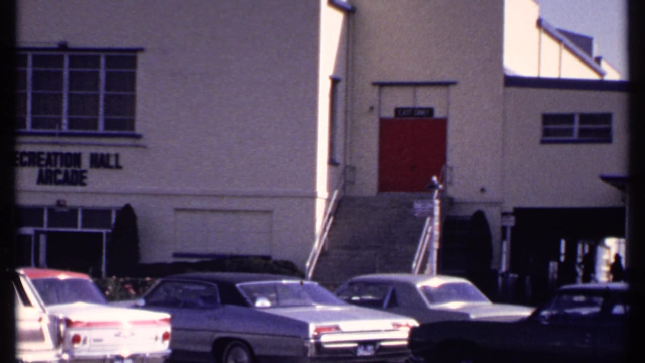 Parking lot with vintage cars outside a recreation hall building with red doors.