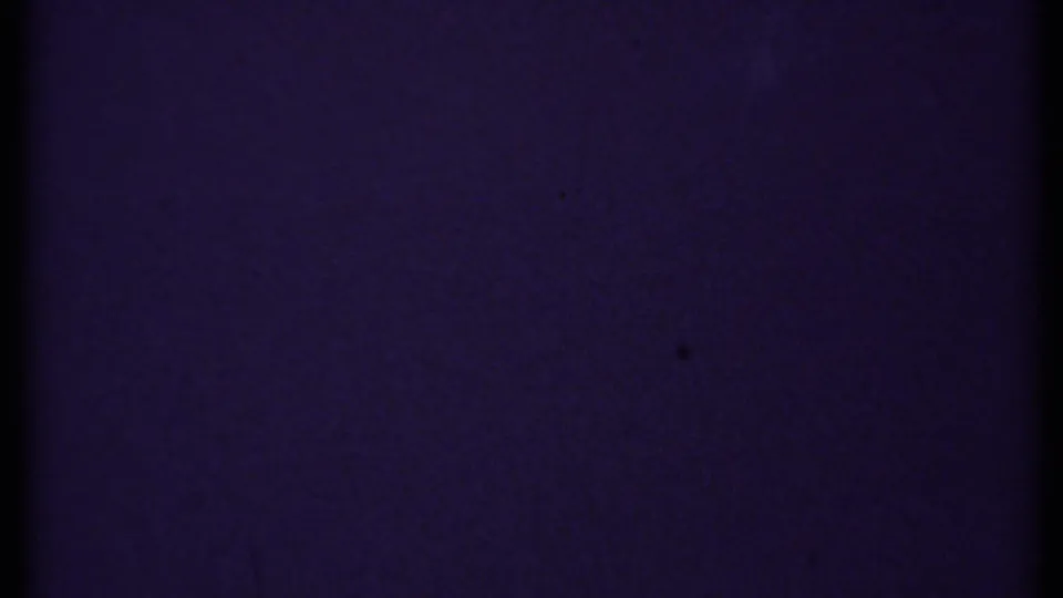 1969 New London 8mm frame showing an indistinct dark blue-purple field with film grain, dust specks, and a black edge from the scan.