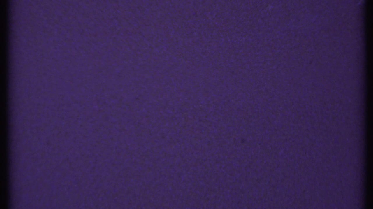 1969 New London 8mm frame with a mostly uniform blue-purple surface, dark gate-edge strip, grain, and faint dust markings.