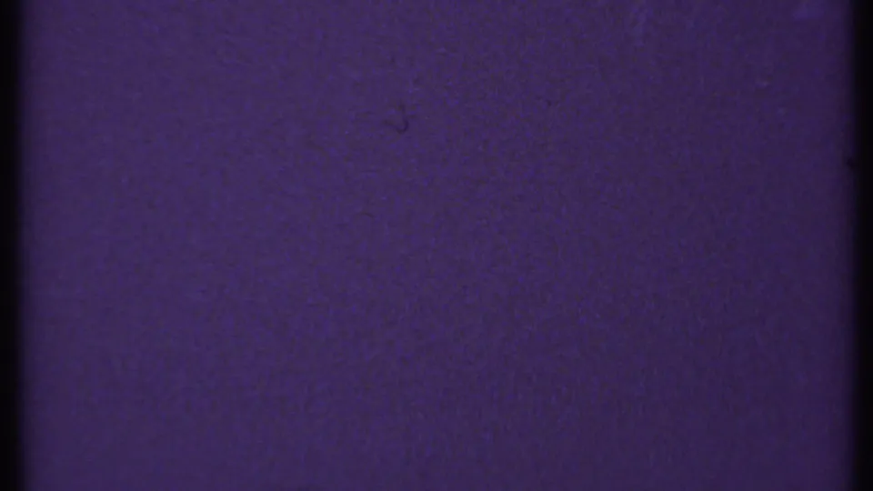 1969 New London 8mm frame showing a lighter blue-purple field with visible grain, faint dust, and the contact-sheet boundary at the top.