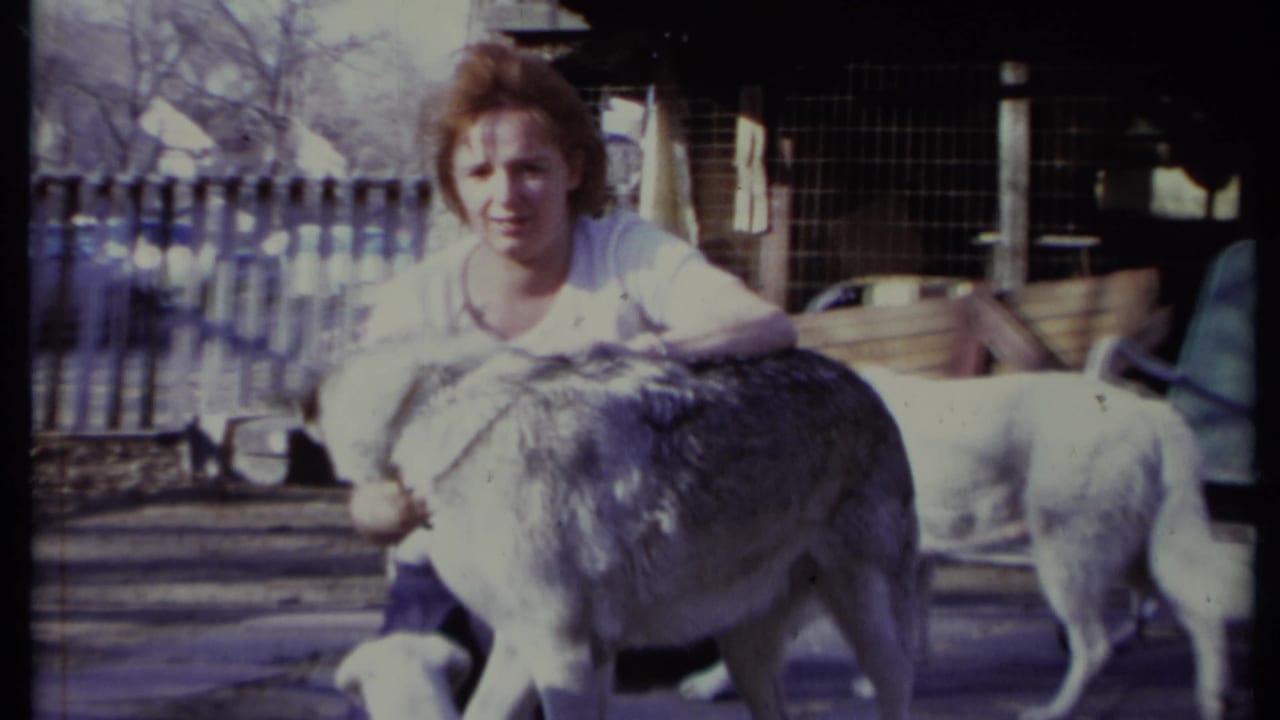 Woman facing camera while petting a gray-and-white dog in a yard.