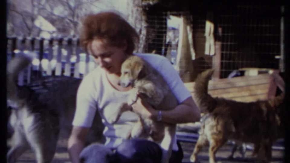 The woman holds the puppy against her chest as a husky-type dog and other dogs stand nearby in the California outdoor setting.