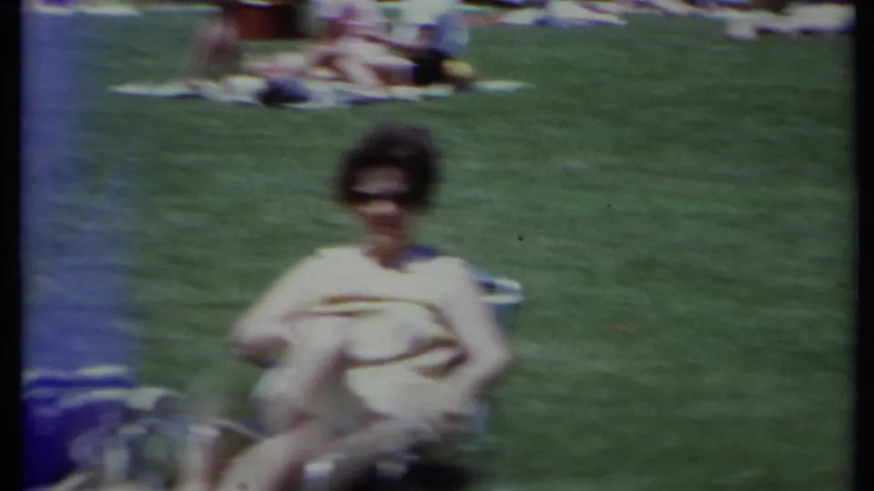 A seated adult wearing sunglasses appears on a lawn in the 1971 California home-movie frame, with the dog partly visible nearby.