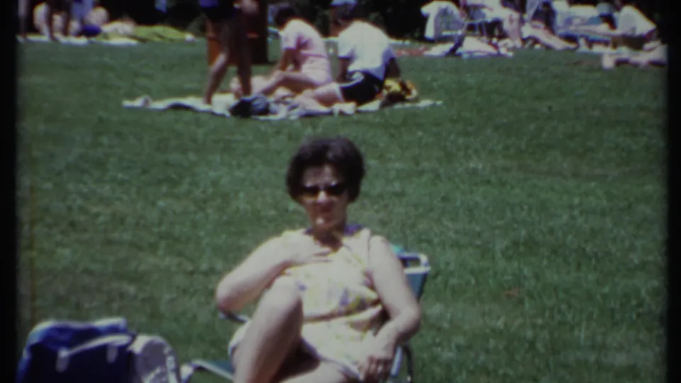 A seated woman faces the camera from a grassy California park as groups lounge on blankets behind her in 1971 footage.