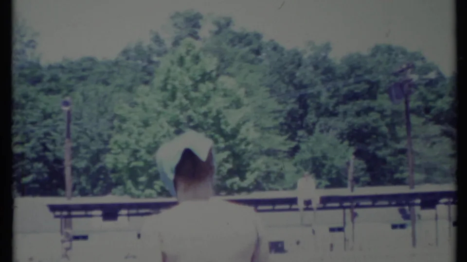 The final frame shows a back-facing figure in a white hat near a low railing or building edge, with trees in soft focus behind.