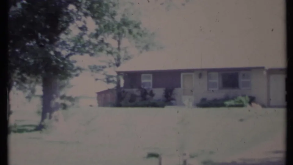 1971 California home-movie frame showing a ranch-style house exterior with a broad lawn, driveway, and tree shade.