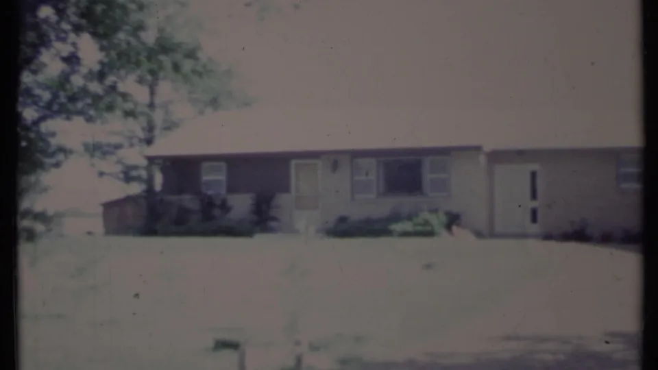 Soft 8mm frame of a California ranch-style house with front lawn, driveway, windows, and overexposed tree shade.