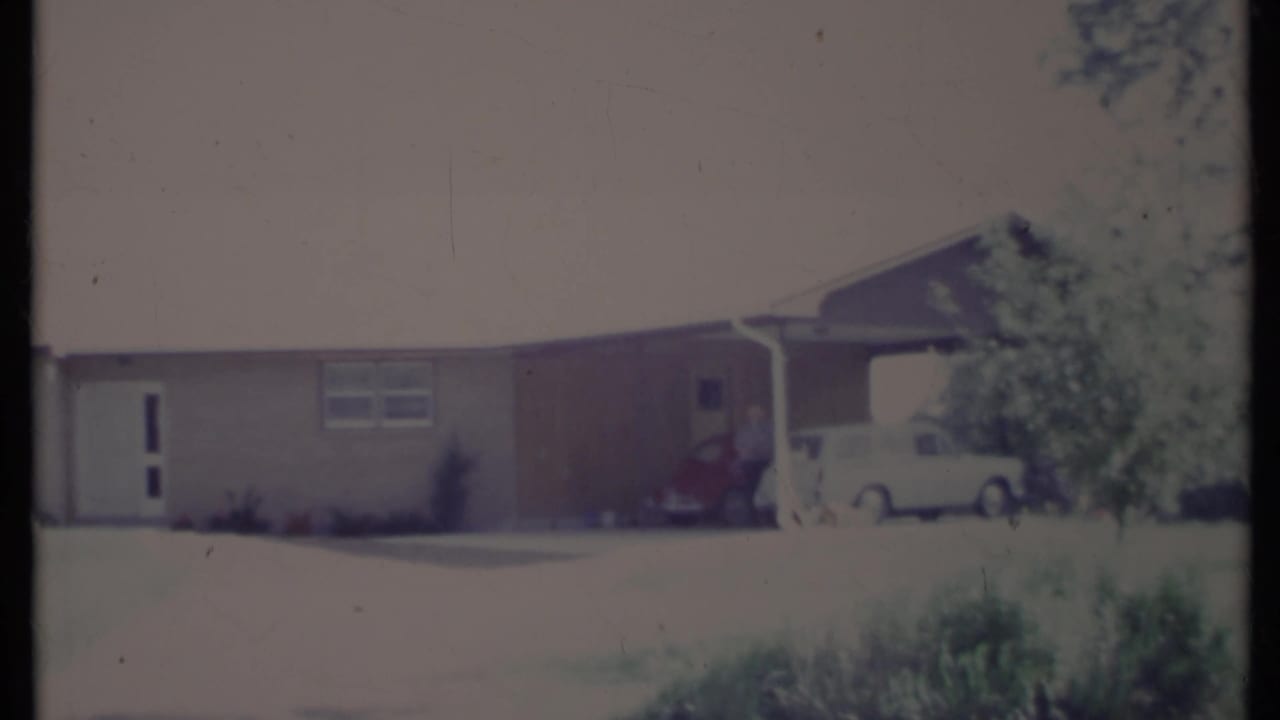 Single-level ranch house with lawn, front window, and cars under a carport.