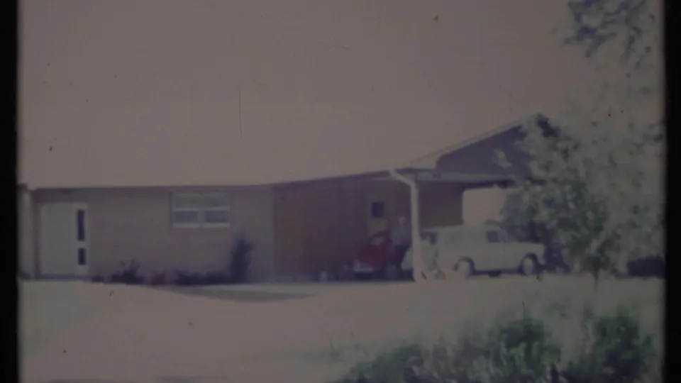 1971 California 8mm frame showing a single-level suburban house with a large front window, lawn, red car, and white wagon near the carport.