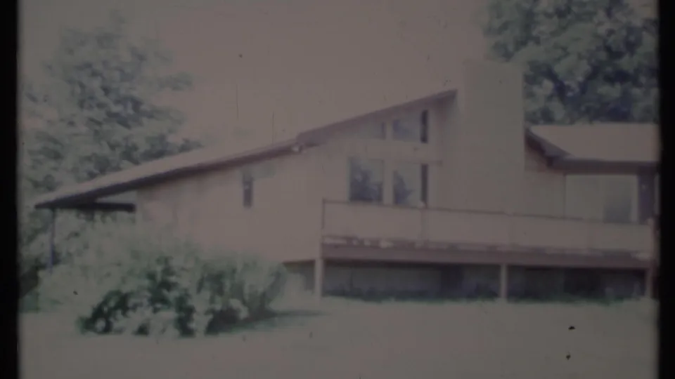 1971 California 8mm frame showing a mid-century house exterior with sloped roof, tall chimney, upper deck, lawn, and trees.