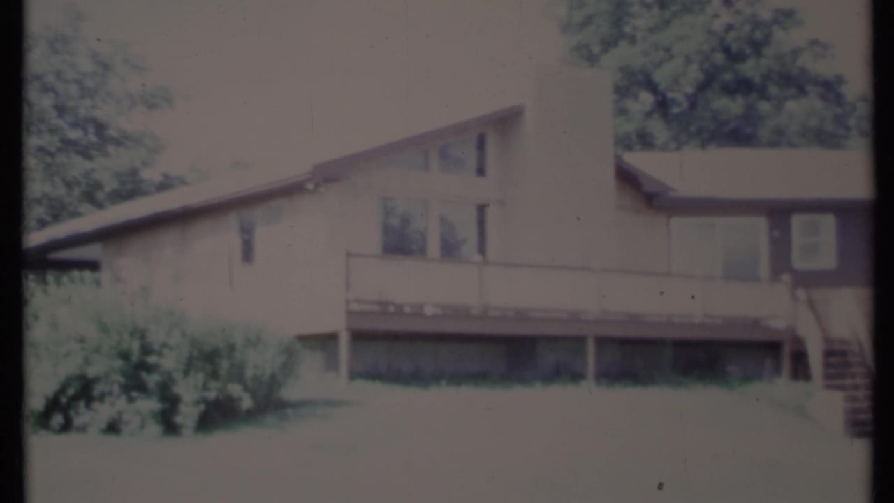 House exterior with sloped roof, deck railing, chimney, windows, and side stairs.