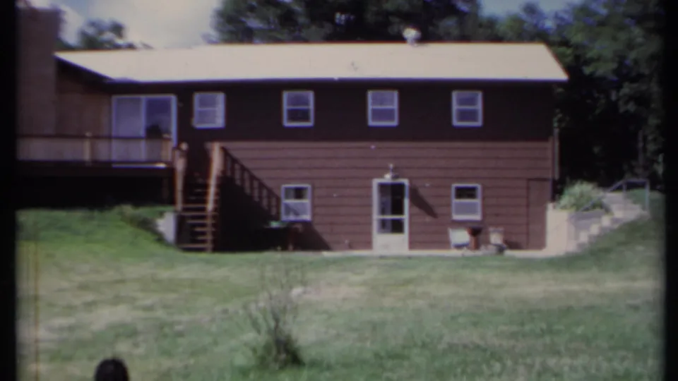 1971 California 8mm frame showing a brown two-story house, deck stairs, lawn, and trees.