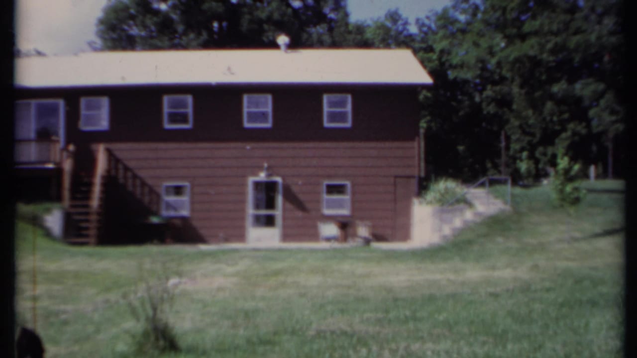 Brown house centered with stairs, windows, lawn, and trees behind it.