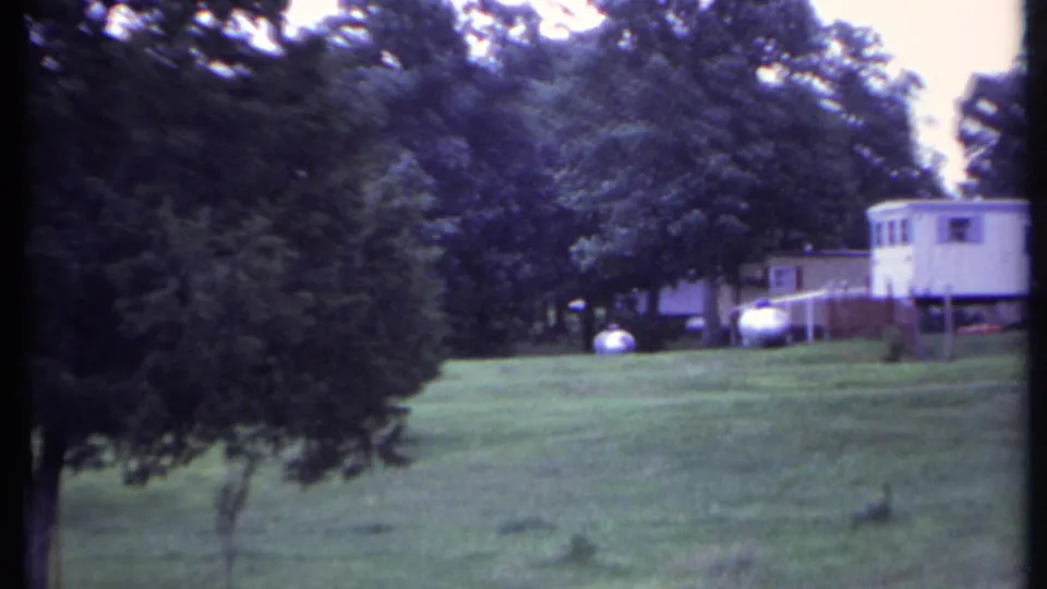 1971 California frame with trees across an open lawn and a white mobile home partly visible near the right edge.
