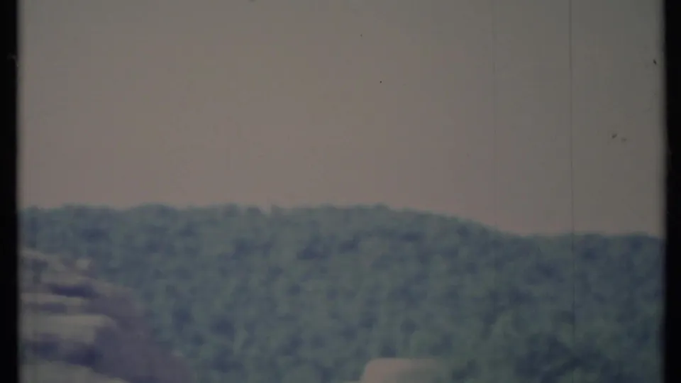 1971 California home-movie frame showing a hazy forested mountain ridge under a gray sky with visible film grain.