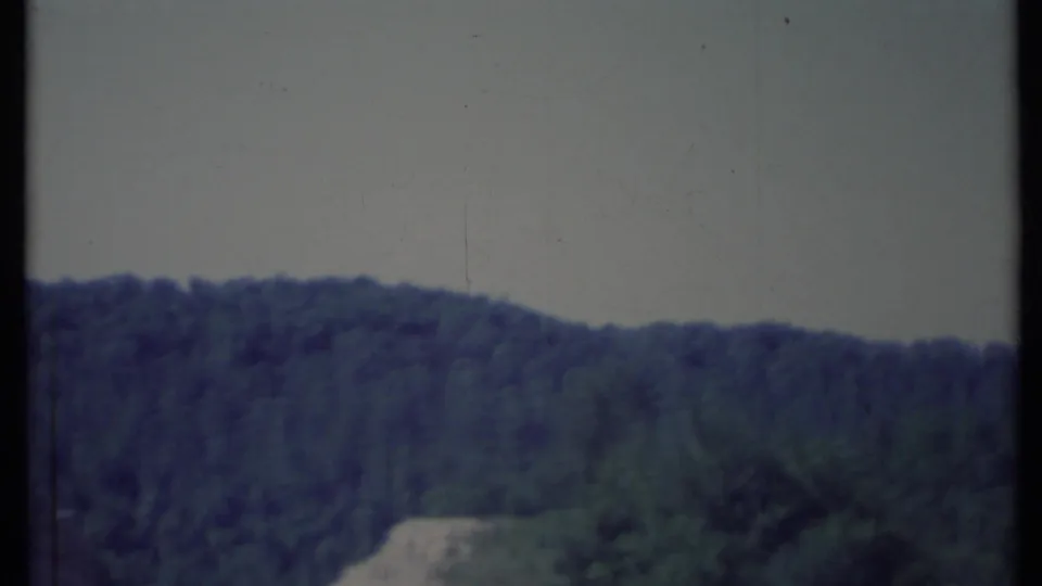 1971 California 8mm frame with a wooded mountain ridge and a faint light strip that appears to be a road or clearing.