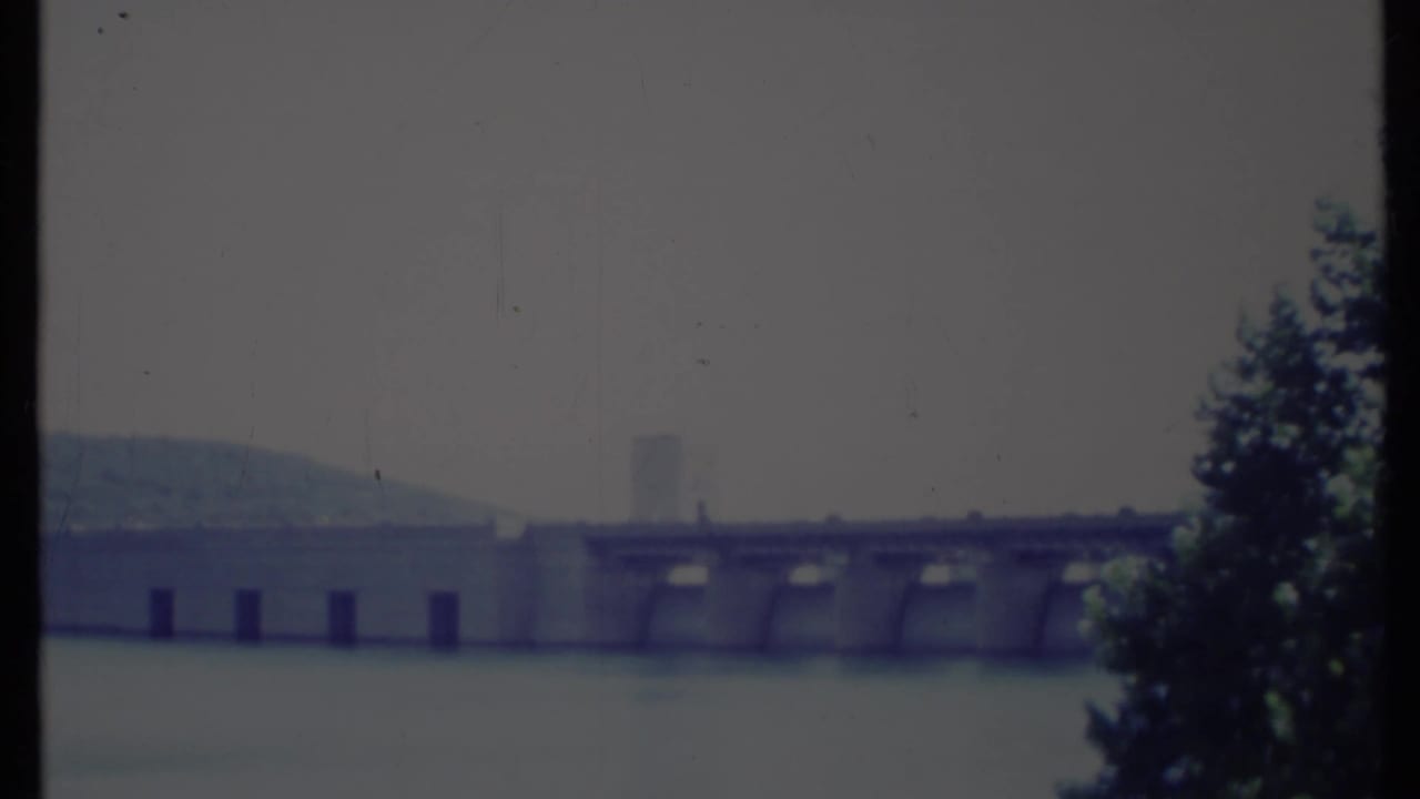 Dam and water viewed through dark vertical film borders with a tree at the right.