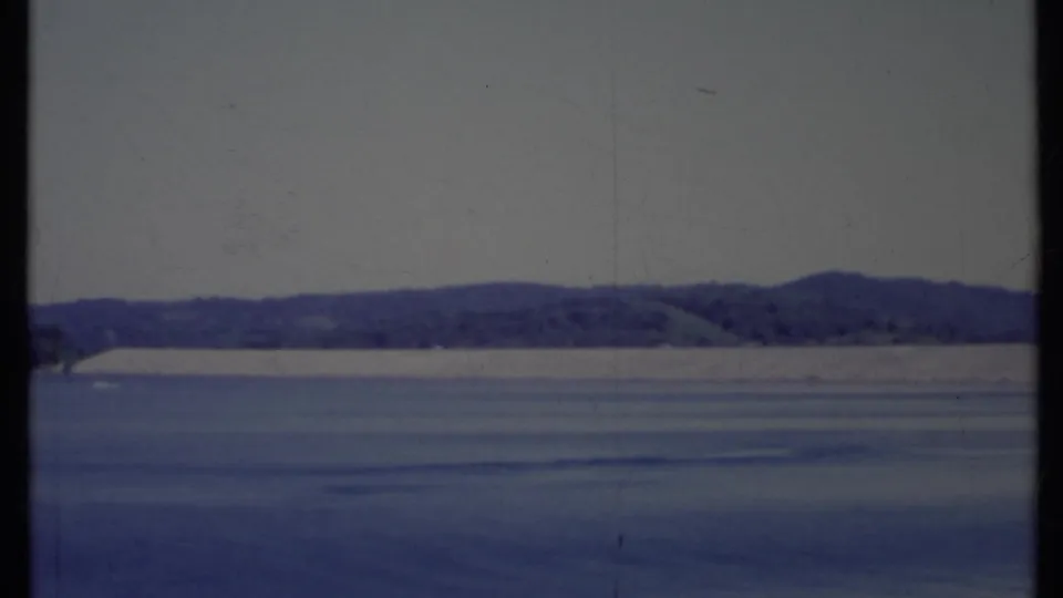 1971 California 8mm view across a quiet bay, with low hills on the horizon and a dark film gate bar crossing the frame.