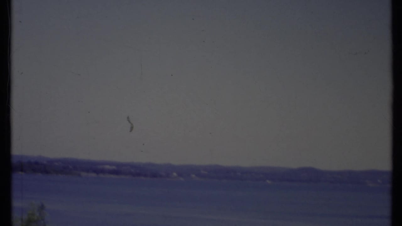 Wide blue water beneath a hazy sky with a distant low shoreline and dark film borders.