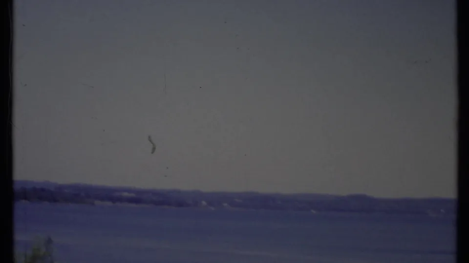 1971 California 8mm frame showing a calm lake or bay, distant shoreline, hazy sky, and visible film edge texture.