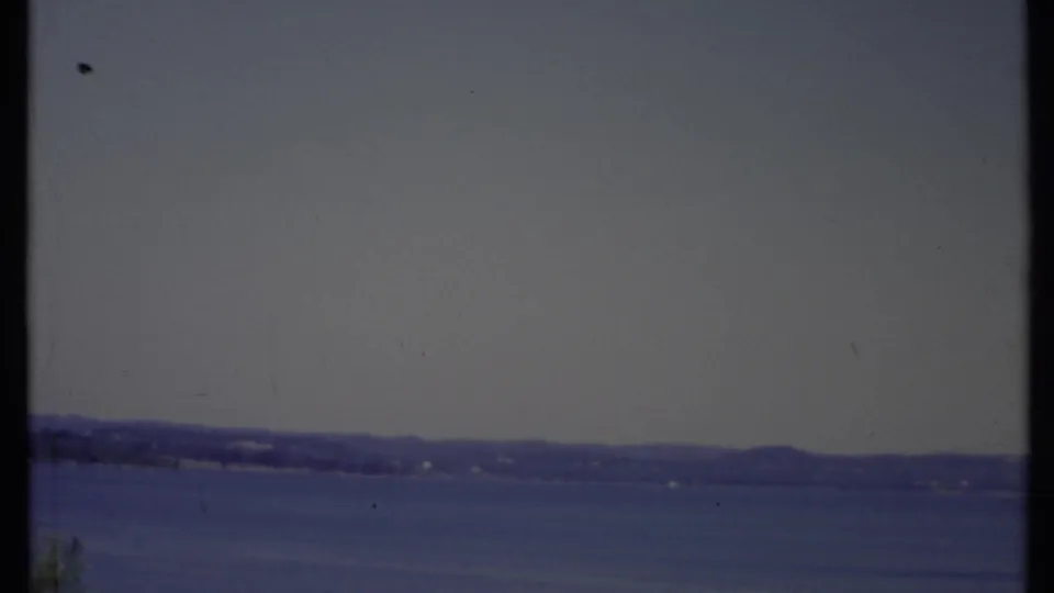 1971 California home-movie frame with broad water, a low far shore, hazy sky, and soft faded 8mm color.