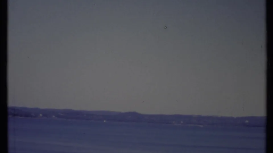 1971 California home-movie frame showing a quiet waterside horizon, soft focus, faded color, and 8mm surface marks.