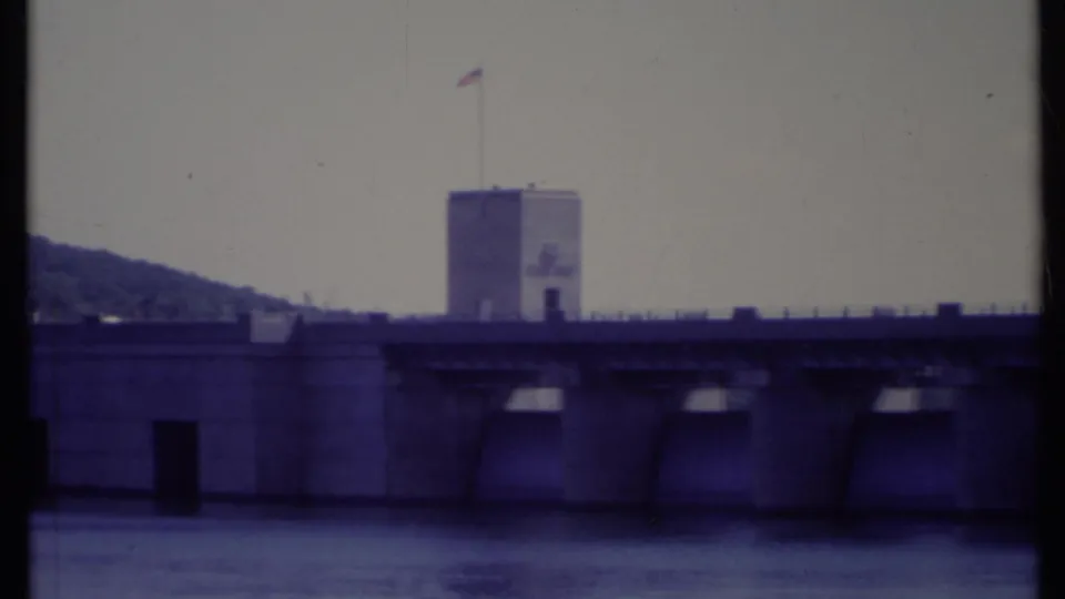 1971 California home-movie view of a large dam and tower with an American flag, filmed across the water.