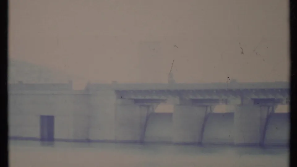 Bright, washed 8mm frame of the California dam, with the tower and spillway supports partly faded by exposure.