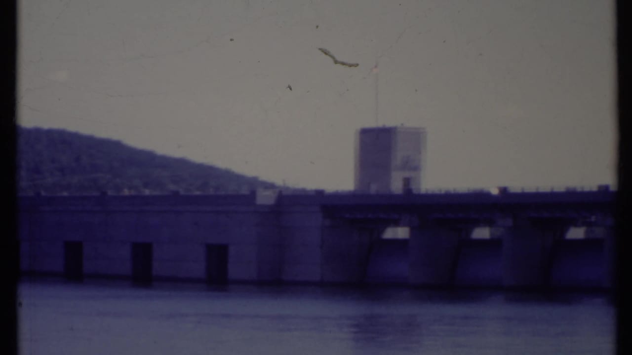 Dam structure across water with a tower and hillside behind it.