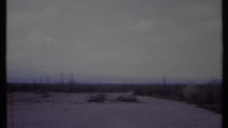 A muted 8mm frame shows California scrubland, a curving dirt path, and thin utility poles receding across the horizon.