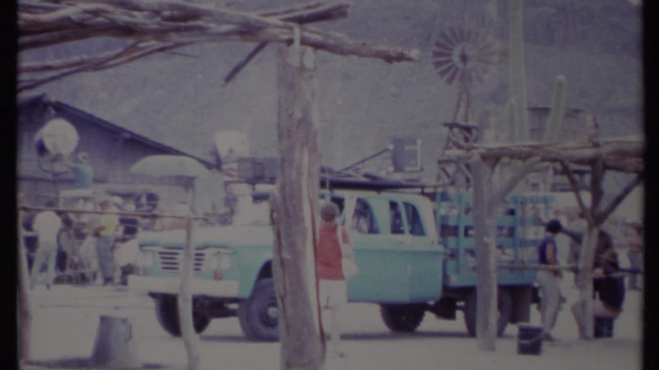 Blue truck and people near a rustic desert set with a reflector and wooden posts.