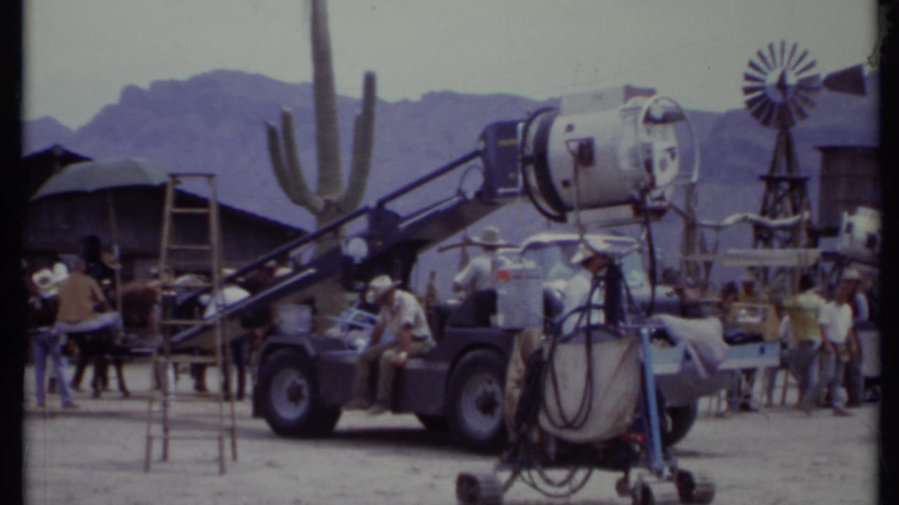 Western film set with crew, lighting truck, cactus, windmill, and desert mountains.