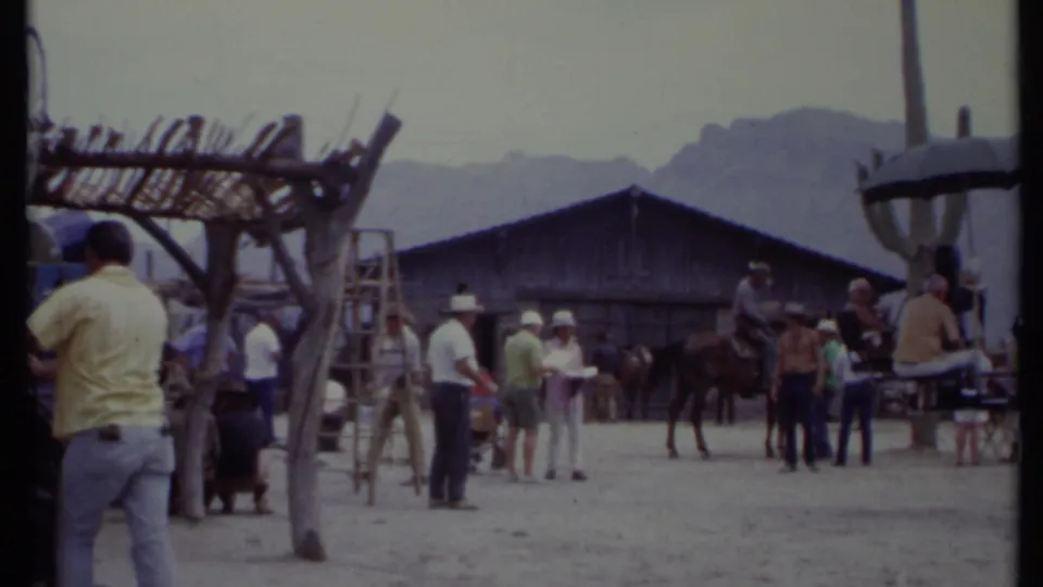 1971 California 8mm frame showing people gathered on a Western set near a horse, ladders, rustic structures, and distant mountains.