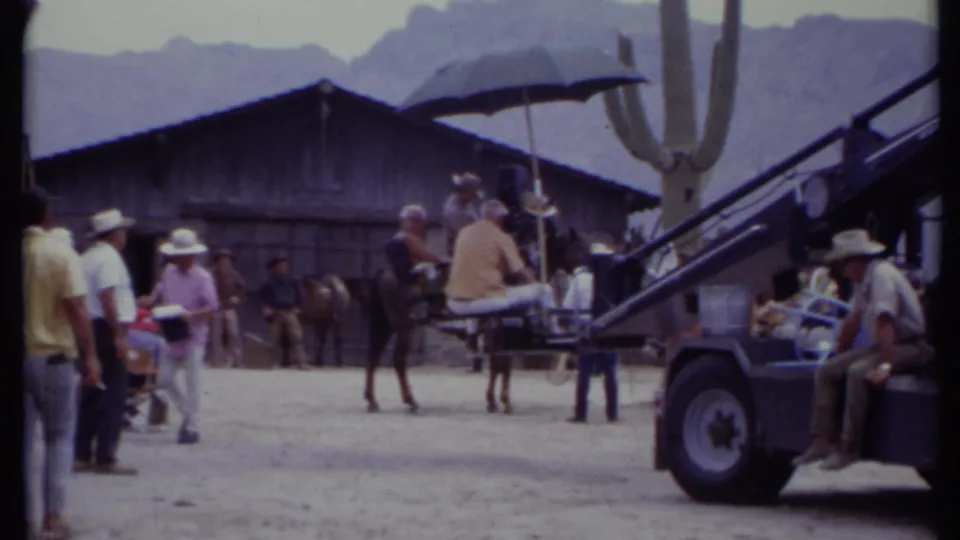 1971 California frame with crew, camera crane vehicle, seated operator, horse, saguaro cactus, and Western-style wooden structure.