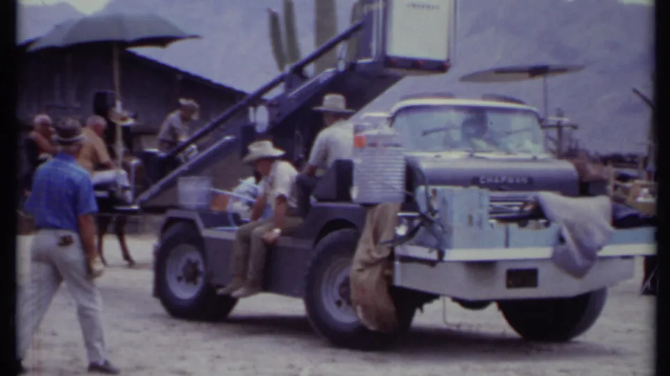 1971 California frame with a visible vehicle front and crane rig beside crew, horse, Western set building, cactus, and distant mountains.