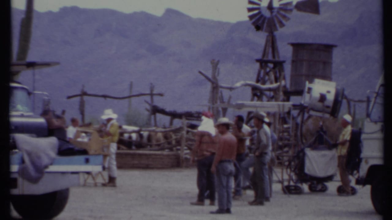 Western set with crew, truck, cactus props, windmill, and mountains in the background.