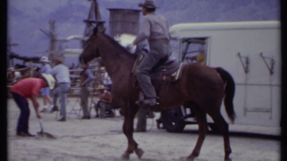 1971 California frame with a horse rider beside a white trailer as crew members work among Western props and vehicles.
