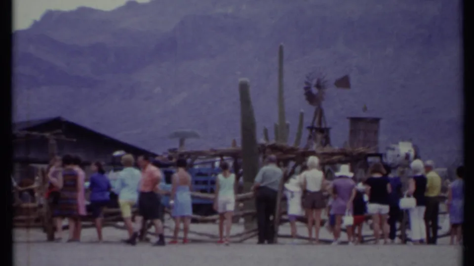 1971 California 8mm frame showing tourists at a Western-themed attraction with cacti, windmill, wooden buildings, mountains, and a white horse figure.