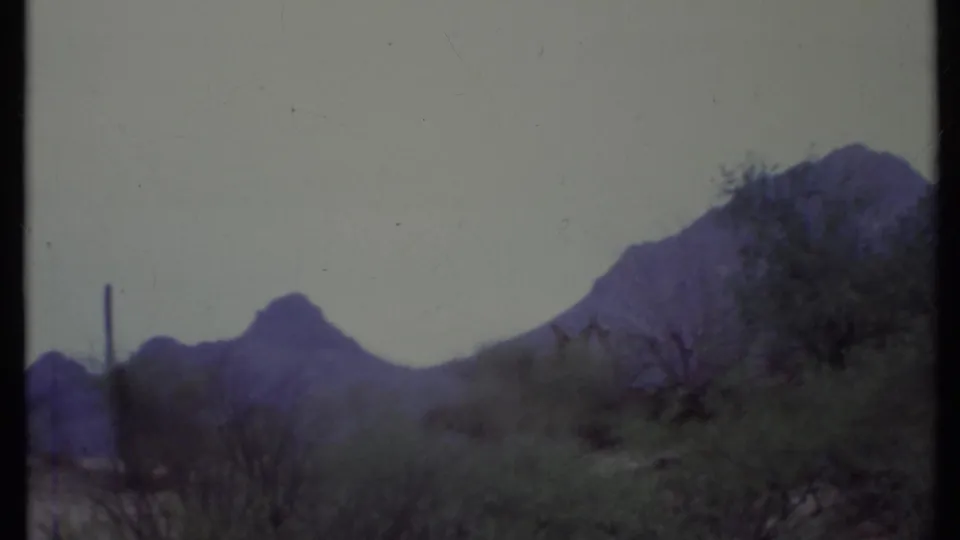 1971 California 8mm frame of an open desert road, sparse bushes, and rugged mountain peaks after the pan has moved away from the truck.