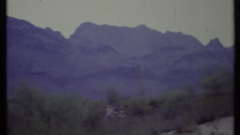 1971 California 8mm frame emphasizing rocky desert mountains, low shrubs, and cactus-like vegetation with a strong blue-purple cast.