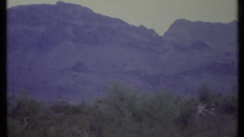 1971 California desert landscape frame with a large mountain slope, sparse foreground plants, and visible 8mm film texture.