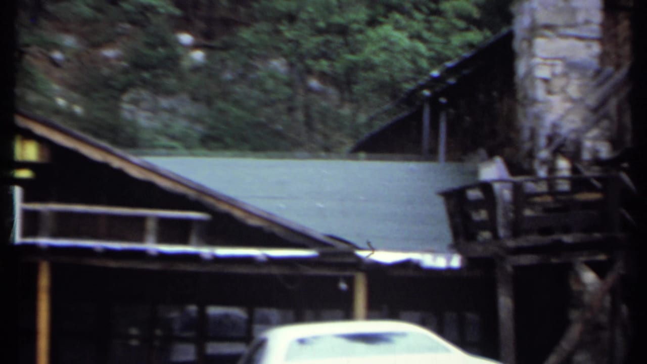 Rustic inn building partly obscured by trees with a white car in the foreground.