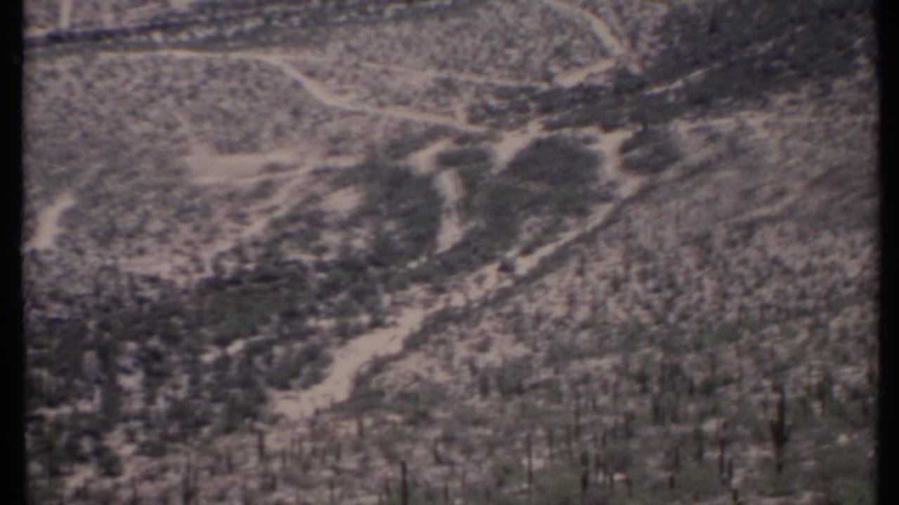 Aerial view of dry desert hills with pale dirt tracks and sparse scrub.