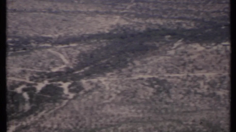 A soft 8mm aerial view over California desert land, showing road cuts, scrub patches, and faded color.