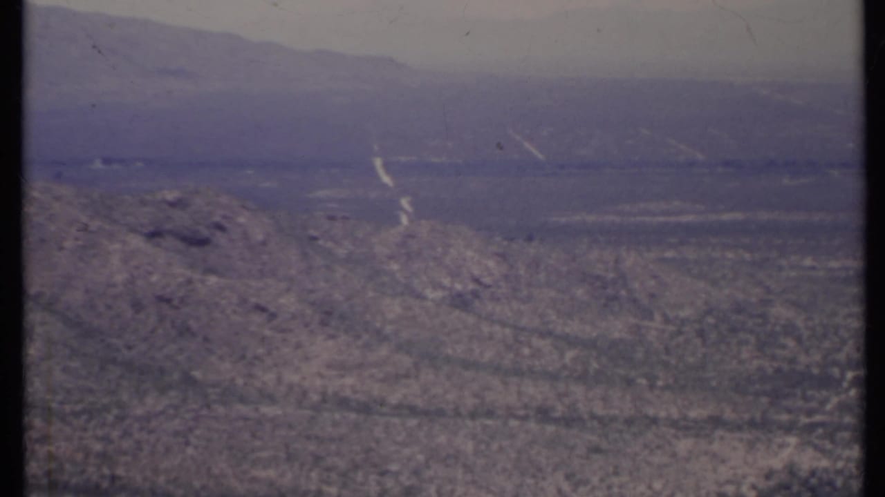 Hazy desert valley with rocky slope and distant mountains.