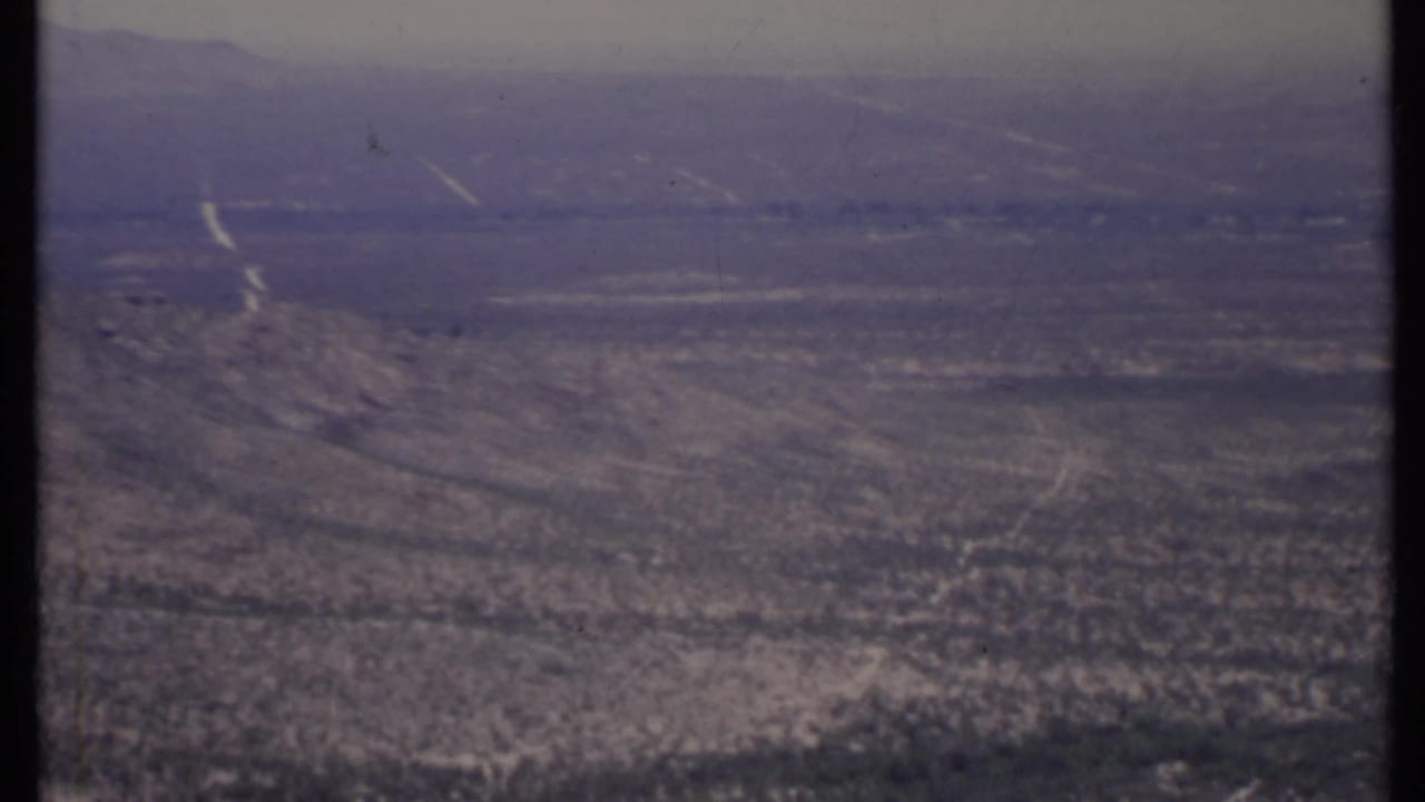 Wide arid landscape with low hills, shrubs, and distant ridges.