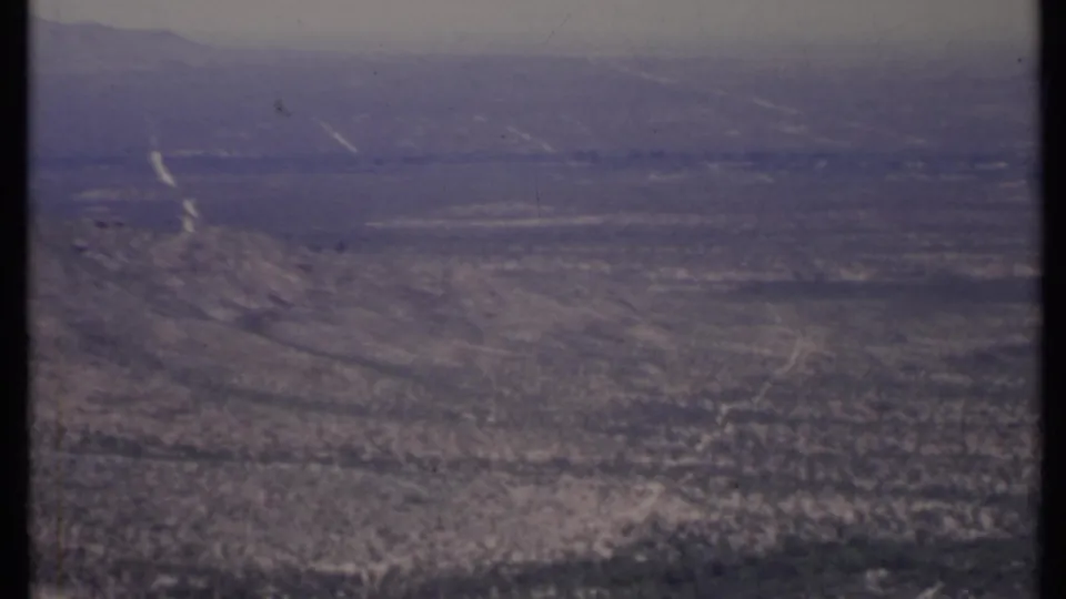 Elevated 1971 California desert view showing low rocky hills, sparse vegetation, faint tracks, and layered ridges under a muted sky.