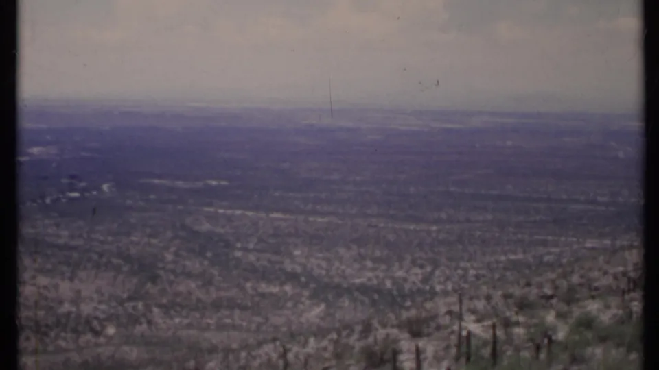 Hazy 1971 California 8mm view across dry terrain, with scrub and cactus in the foreground and a wide muted horizon beyond.